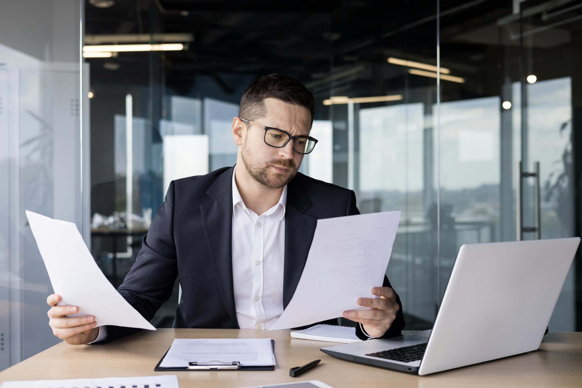 A worried young man businessman, accountant reviews documents, business agreements, bills in the