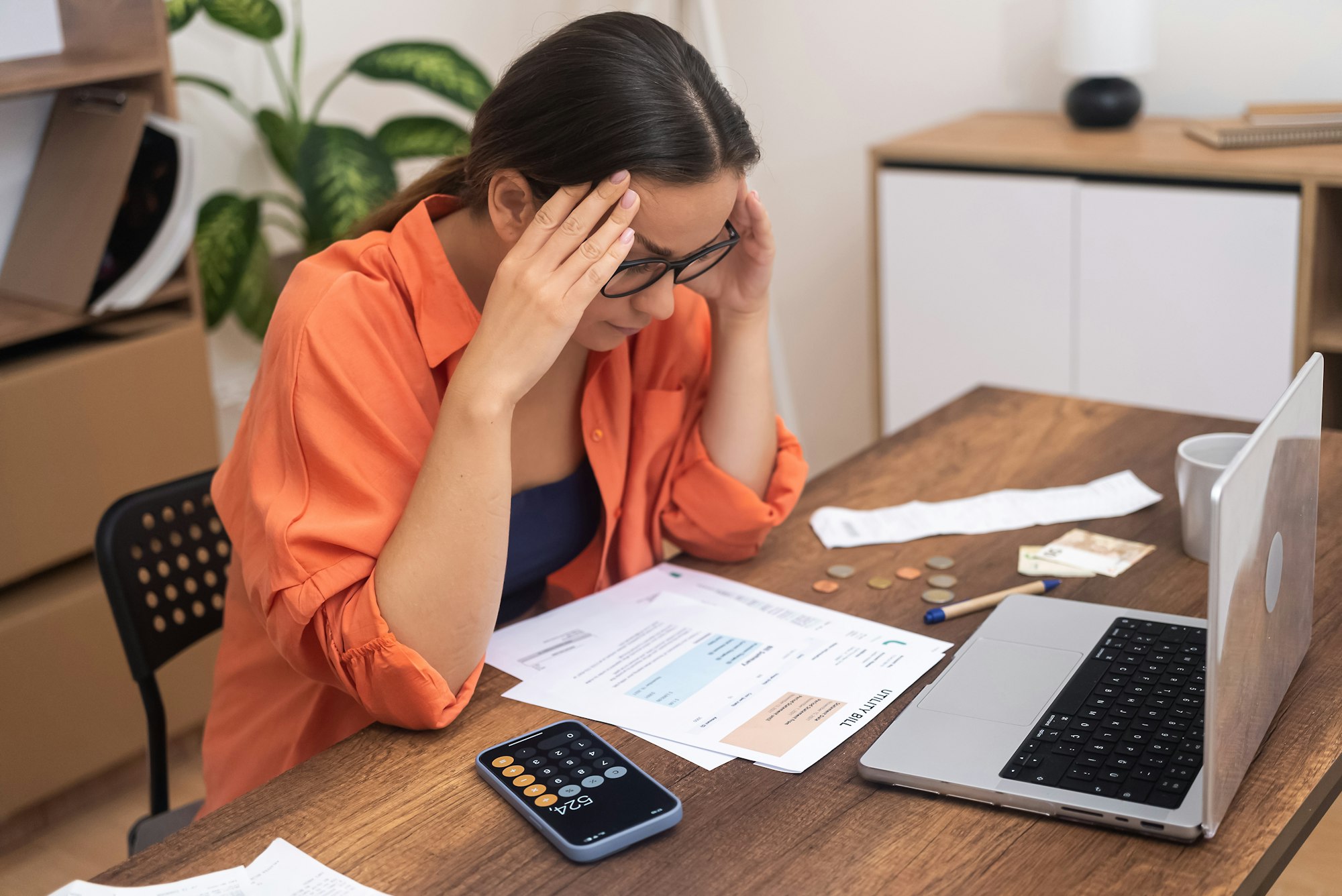 stressed woman at a table looks at paper bills, perplexed by the high payment rates.